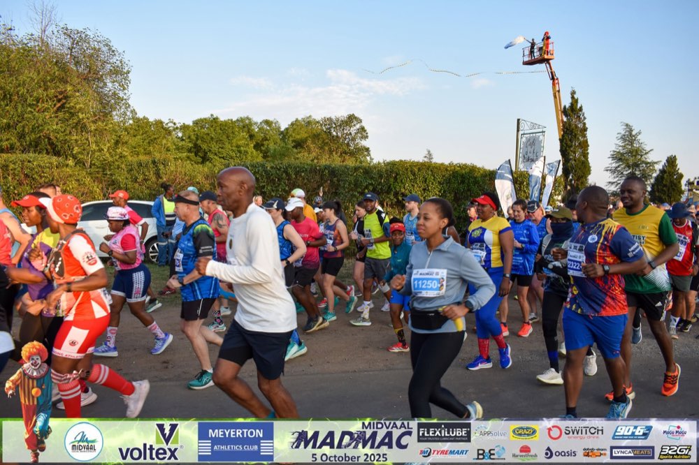 Runners at the MadMac start line in 2025, with Café du Cirque's sign and the club's clown mascot in the foreground